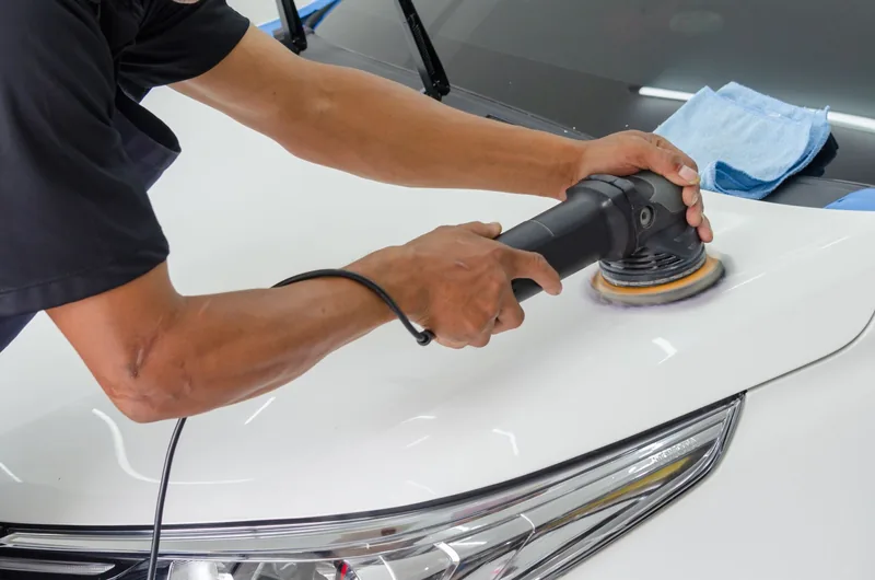 Auto detailer polishing the hood of a white car
