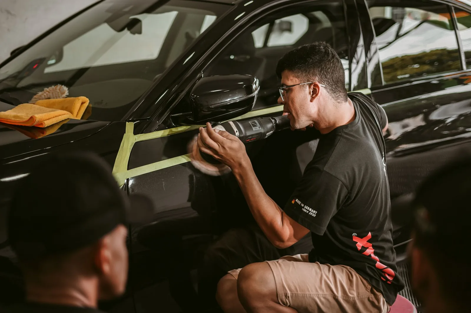 Car detailer machine-polishing the door of a dark car