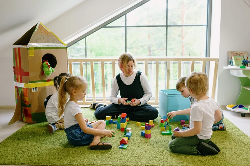 Caregiver building with blocks alongside two children