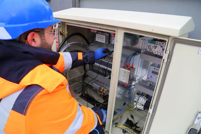 Electrician in a safety helmet servicing an outdoor electrical cabinet