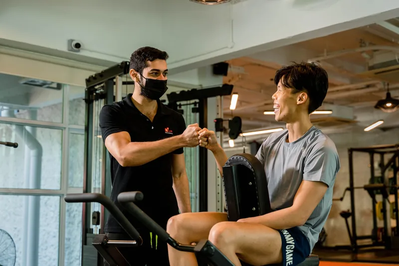 Personal trainer fist-bumping a smiling client in a gym