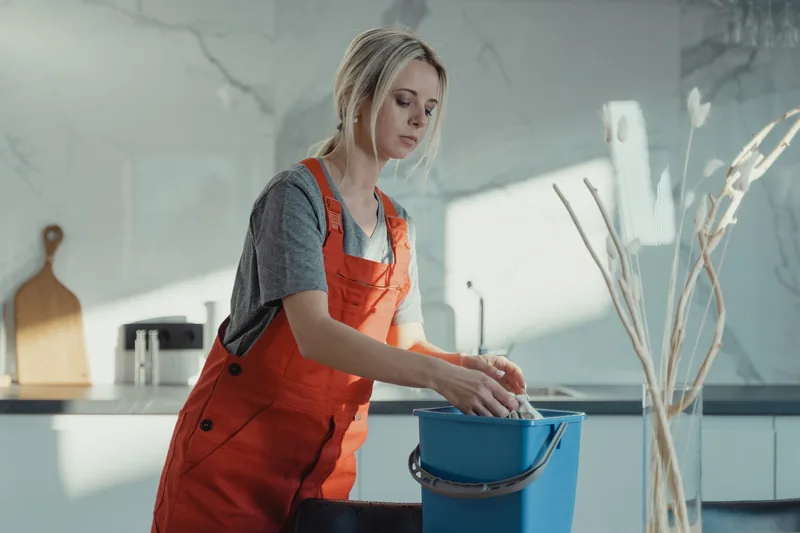 House cleaner wiping a kitchen counter with a bucket nearby