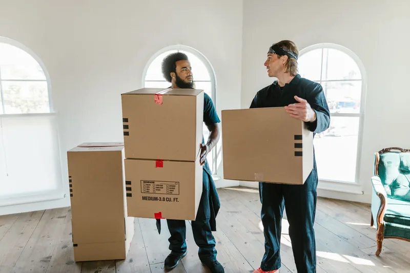 Two movers carrying boxes through a bright home