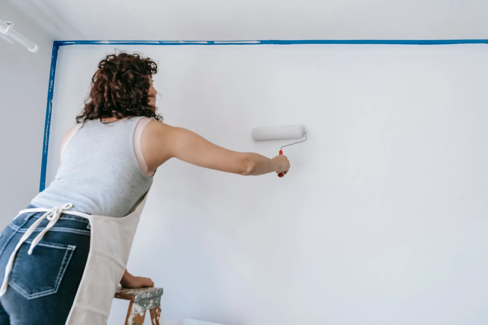 Painter on a ladder rolling white paint onto a wall