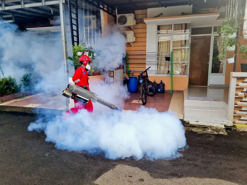 Especialista fumigando con nebulizador el exterior de una casa